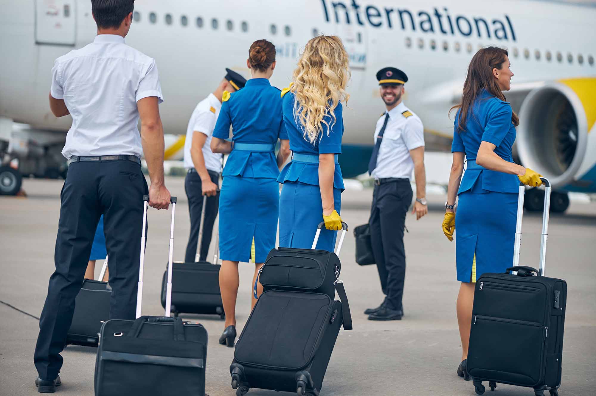 Stewardesses and pilots carrying travel bags at airport with passenger airplane on background